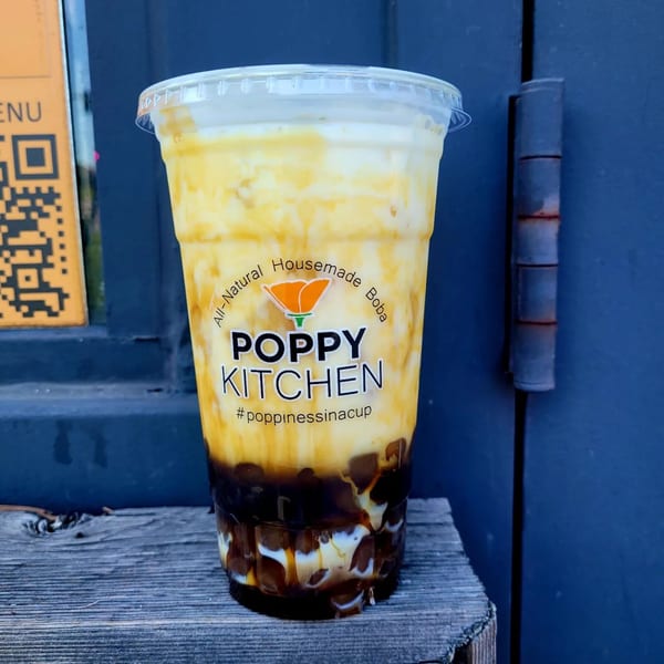 Poppy Boba Kitchen's brown sugar boba drink with creamy white and caramel swirls on a wooden surface.