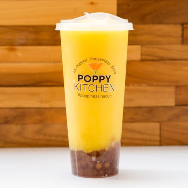 A tall plastic cup of Poppy Kitchen boba tea with yellow liquid and dark brown boba pearls.