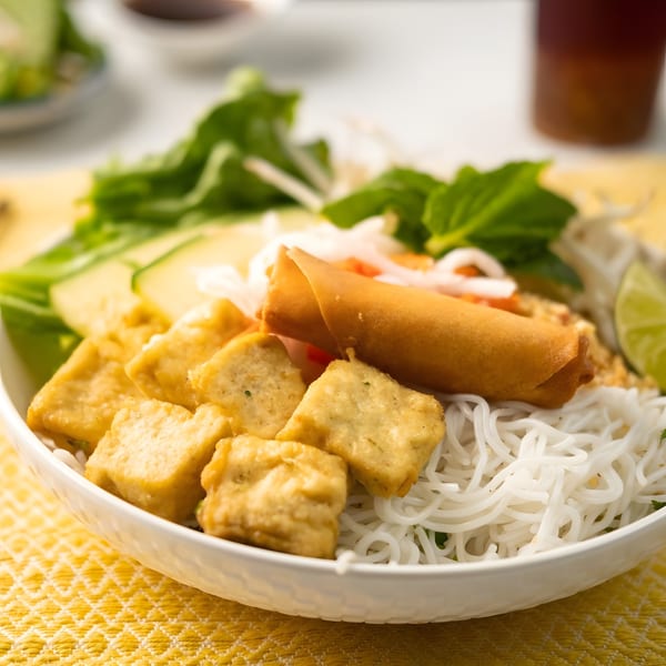 Vietnamese vermicelli noodle bowl with crispy tofu, a fried spring roll, and fresh herbs.