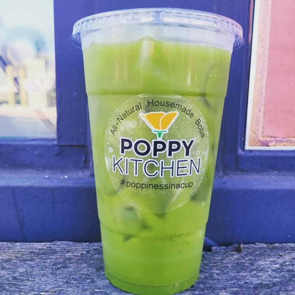 A vibrant green boba drink from Poppy Boba Kitchen with ice, on a wooden surface.