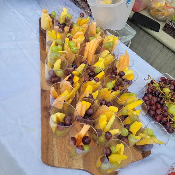 Individual cups filled with fresh mango, cantaloupe, red grapes, and green grapes on a wooden board.