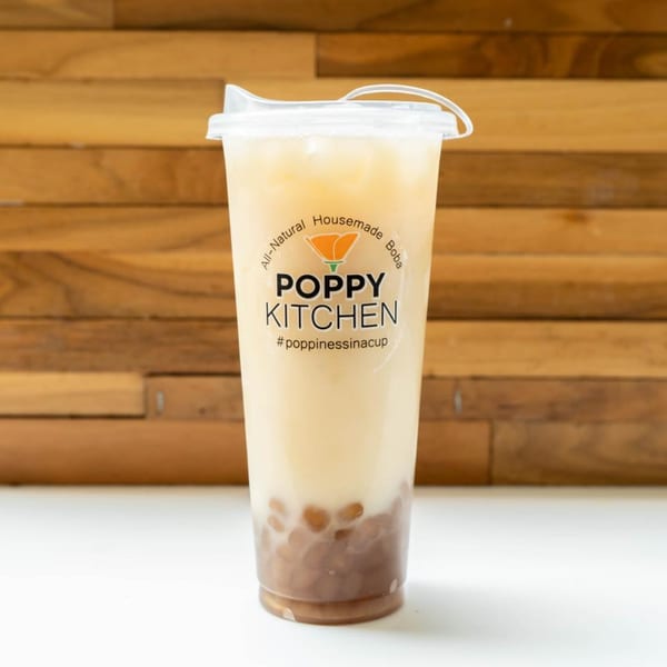 A Poppy Kitchen boba tea with tapioca pearls and a light-colored drink against a wooden background.