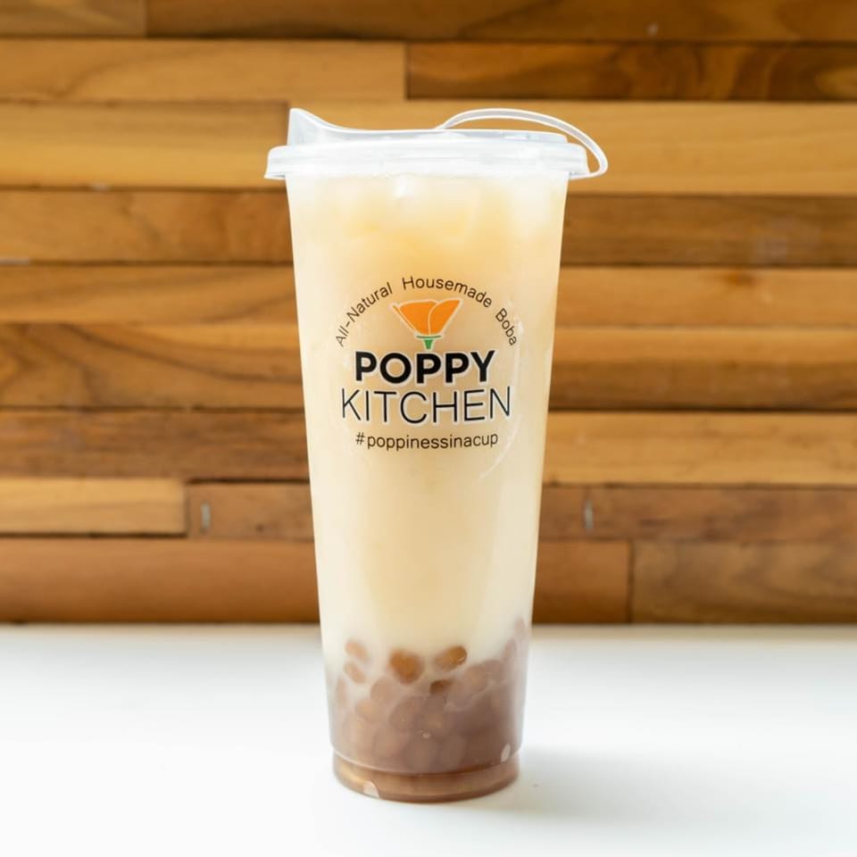 A Poppy Kitchen boba tea with tapioca pearls and a light-colored drink against a wooden background.