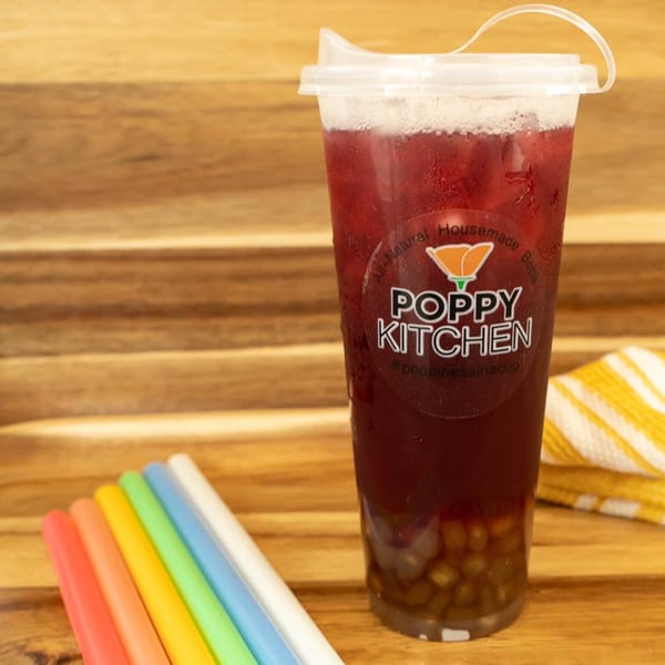 Poppy Boba Kitchen's red boba tea with tapioca pearls, rainbow straws, and a yellow towel on wood.