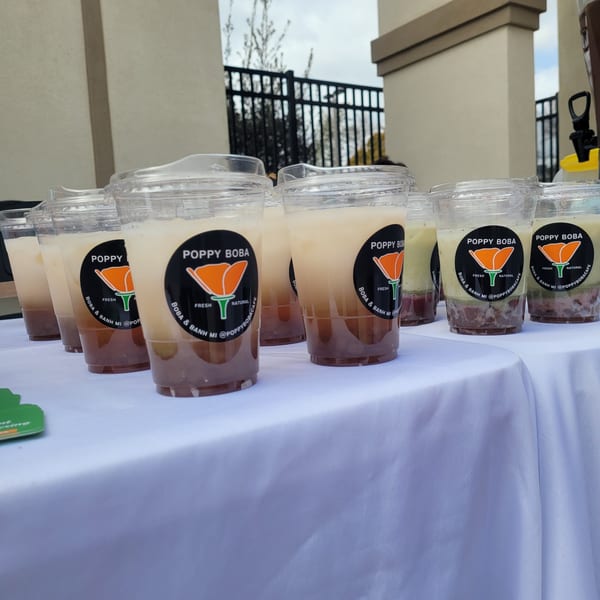 Rows of Poppy Boba Kitchen drinks with layered ingredients and branded stickers on a white tablecloth.