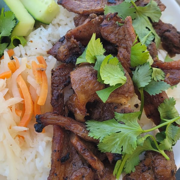 Close-up of Vietnamese grilled pork with rice, pickled carrots, daikon, cucumber, and cilantro.