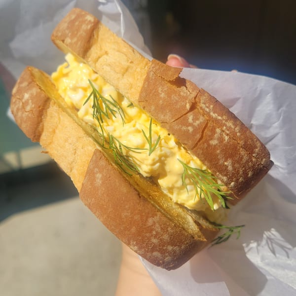 Close-up of a Vietnamese egg salad sandwich with dill, held in white paper.